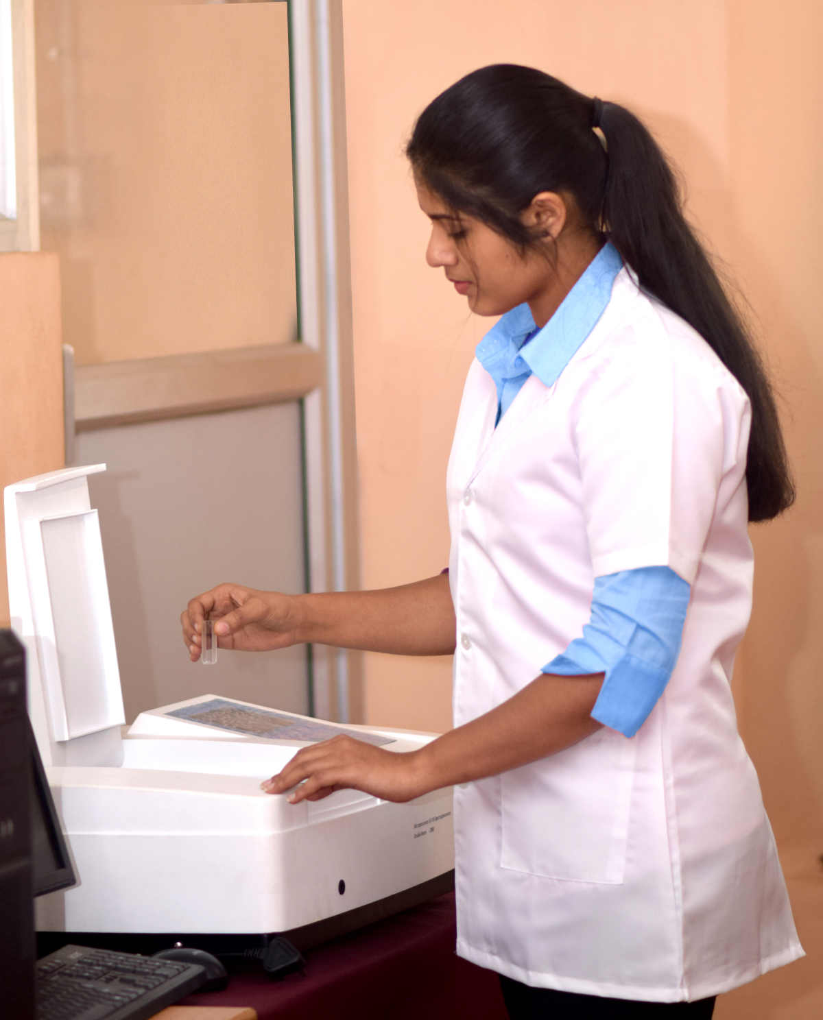 Rosemary Salin is using a UV-Visible Spectrometer. A cuvette containing a sample for analysis is being loaded into the spectrometer.